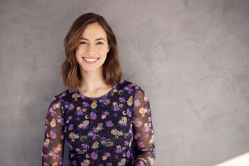 Portrait of a brunette caucasian woman smiling and looking beautiful standing isolated over grey concrete background. Elegant and attractive young female girl looking happy in camera.