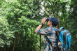 Tourist is watching bird on top of tree through binoculars in jungle. Travel, Hiking, Trekking concept.