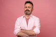 Portrait of doubtful man in pastel pink shirt on pink wall. Middle age grey-haired beard man with crossed hands thinking about question, pensive expression. smiling with thoughtful face. doubt concept