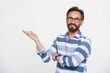 Bearded happy smiling caucasian man 40s wear stiped blue-white shirt and glasses point hand with empty palm at copy space place isolated on white background studio portrait. People lifestyle concept