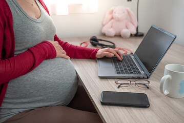 Cropped image of beautiful pregnant business woman typing with one hand holding other hand on her belly while finishing working from home. Maternity or parental leave