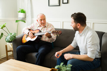 Wall Mural - Senior caucasian man enjoying music and playing the guitar with his son