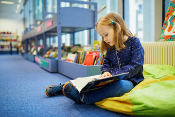 4 year old girl sitting on the floor in municipal library and reading a book