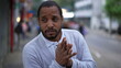 © Marco - One anxious black man standing in urban street feeling nervous and stressed. Desperate African American rubbing hands in anxiety in modern sidewalk