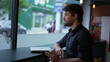 © Marco - Pensive young entrepreneur thinking by window looking at city sidewalk lost in thought. One thoughtful man daydreaming