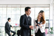 © artitwpd - Senior Asian businessman and young female businesswoman discuss in the office, working on social media strategy, looking at a tablet with blur colleagues in the background. Image with copy space.