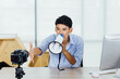 © AllieGraphix - Young Asian businessman using megaphone while looking at the camera.