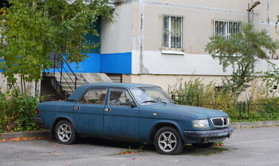 An old rusty blue car is parked near a residential building, Kollontai Street, St. Petersburg, Russia, October 2022