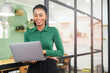 © Vadim Pastuh - Smart and intelligent African-American businesswoman wearing smart casual shirt using laptop indoors, female office employee holding computer and typing message, smiling, enjoying her job