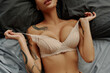top view of cropped tattooed woman with sexy bust lying on bed and taking off beige bra.