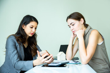 Two expertise business women in well dressed are checking the selling and interest about the property on internet by using electronic device in the office background. Business concept with copy space.