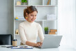 © amnaj - Portrait of smiling Asian businesswoman enjoying her work on her laptop at the office.