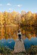 © Наталья Анюхина - A young girl in a hat stands on a bridge near a pond in an autumn landscape