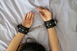 Sexy lady in bdsm outfit. submissive girl in leather handcuffs lying on a white sheet in the bedroom. The concept of BDSM sex submission and domination.