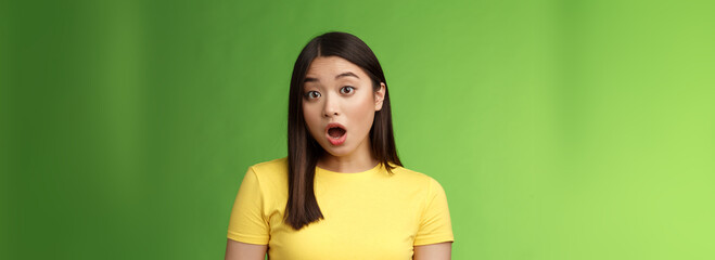 Close-up shocked amazed asian brunette female astonished hear stunning gossip, drop jaw stare camera speechless stand stupor green background, surprised what happening, wear yellow t-shirt