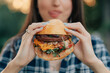 © MZaitsev - Young attractive hungry woman bites a big hamburger outdoor. Close up.
