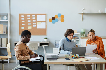 Wall Mural - Side view portrait of black young man with disability working in office during diverse business team meeting