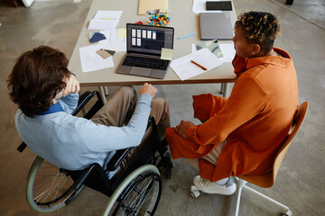 Top view of young man with disability talking to colleague or manager while working in IT development company, accessible jobs concept