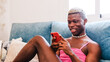 African Black transsexual man in stylish feminine clothes texting on cellphone on couch