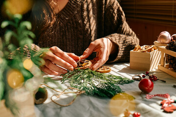 Wall Mural - Woman making Christmas arrangement with fir branches and dried oranges. Female hands creating Christmas craft handmade decor. New year celebration. Winter holidays.