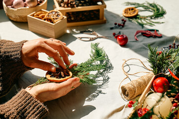 Wall Mural - Woman making Christmas arrangement with fir branches and dried oranges. Female hands creating Christmas craft handmade decor. New year celebration. Winter holidays.