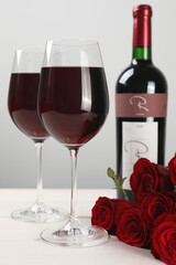 Sticker - Bottle and glasses of red wine near beautiful roses on white wooden table