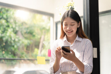 Wall Mural - A beautiful young asian woman holding and using mobile phone.