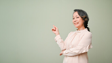 Wall Mural - Happy 60s retired asian woman smiling and standing isolated over green studio background.