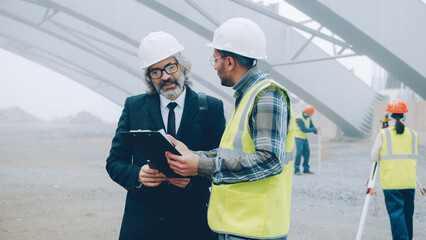 Wall Mural - Project manager is talking to builder discussing construction work in buiding area and using tablet. People and business communication concept.