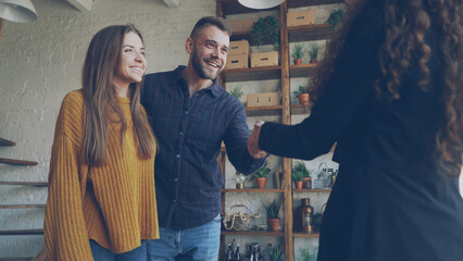 Wall Mural - Married couple is buying appartment, shaking hands with female real estate agent . Relocation, happiness and accommodation concept.