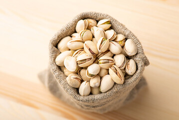 Wall Mural - Small linen bag with pistachios on wooden table. Beautiful composition of pistachios, salted fresh nuts in bag