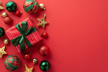 New Year concept. Top view photo of red giftbox with green ribbon bow baubles and gold star ornaments on isolated red background with copyspace