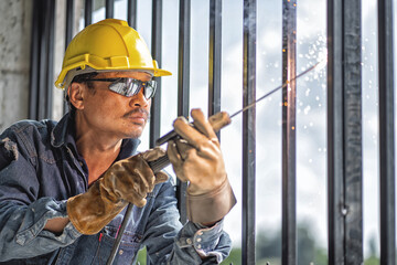 Wall Mural - Asian handyman welding and grinding steel at his workplace As sparks flew around him. He wears a helmet and eye protection.