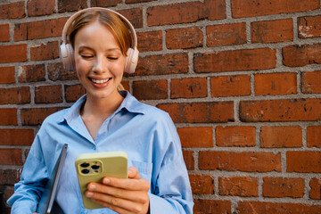 Wall Mural - Young white woman in headphones listening music while using cellphone