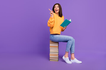 Wall Mural - Full body size photo of charming attractive girl wear orange shirt reading new book literature finger point empty space isolated on violet color background