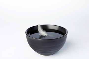 Wall Mural - Water with feather in black bowl on white background