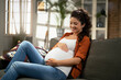 © JustLife - Pregnant woman sitting on a sofa and caressing her belly.