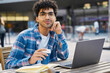 © Maria Vitkovska - Portrait of young man freelancer using laptop computer working online holding cup of coffee. Middle eastern student studying looking at the camera, online education concept