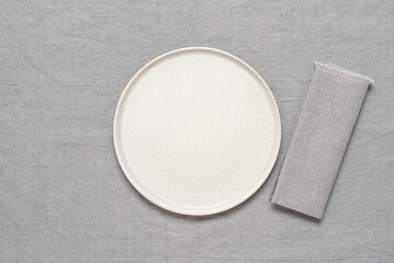 Empty beige plate mockup with gray linen napkin on gray linen tablecloth. Top view, flat lay, copy space.