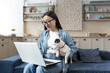 © Liubomir - Young beautiful asian woman at home sitting on sofa and talking on video call using laptop, woman with pet puppy jack russell terrier talking with friends remotely.