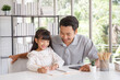 © aekkorn - Children education and home school concept : Young asisn father pleased to see little daughters' study success. Excited smiling small child girl enjoying learning and writing with pleasant dad at home