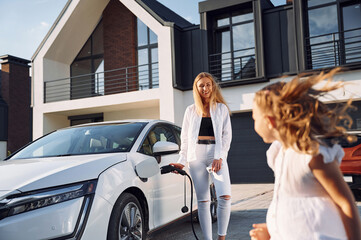 Young woman with her little daughter is with their electric car outdoors