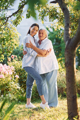 Embracing and posing for a camera. Young woman is with her senior mother is in the garden