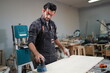 © FotoArtist - Contemporary Carpenter Working, Portrait of modern carpenter making wood furniture while working in joinery lit by sunlight with factory background on small business concept, copy space