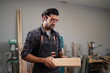 © FotoArtist - Contemporary Carpenter Working, Portrait of modern carpenter making wood furniture while working in joinery lit by sunlight with factory background on small business concept, copy space