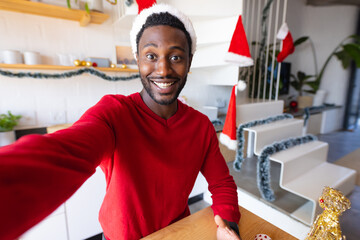 Wall Mural - Happy african american man wearing santa claus hat and having video call