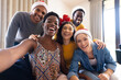 © WavebreakMediaMicro - Image of happy diverse friends celebrating christmas at home taking selfie