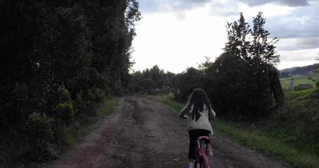 tracking shot of a young girl riding her bike down an uneven dirt road