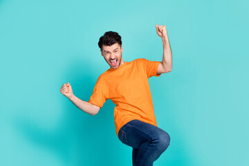 Poster - Photo of young handsome funny excited positive man student wear denim jeans orange t-shirt fists up celebrate win new vacancy isolated on cyan color background