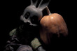 The face of a scary white toy rabbit with red eyes next to a large orange pumpkin. Creepy bunny and big yellow pumpkin